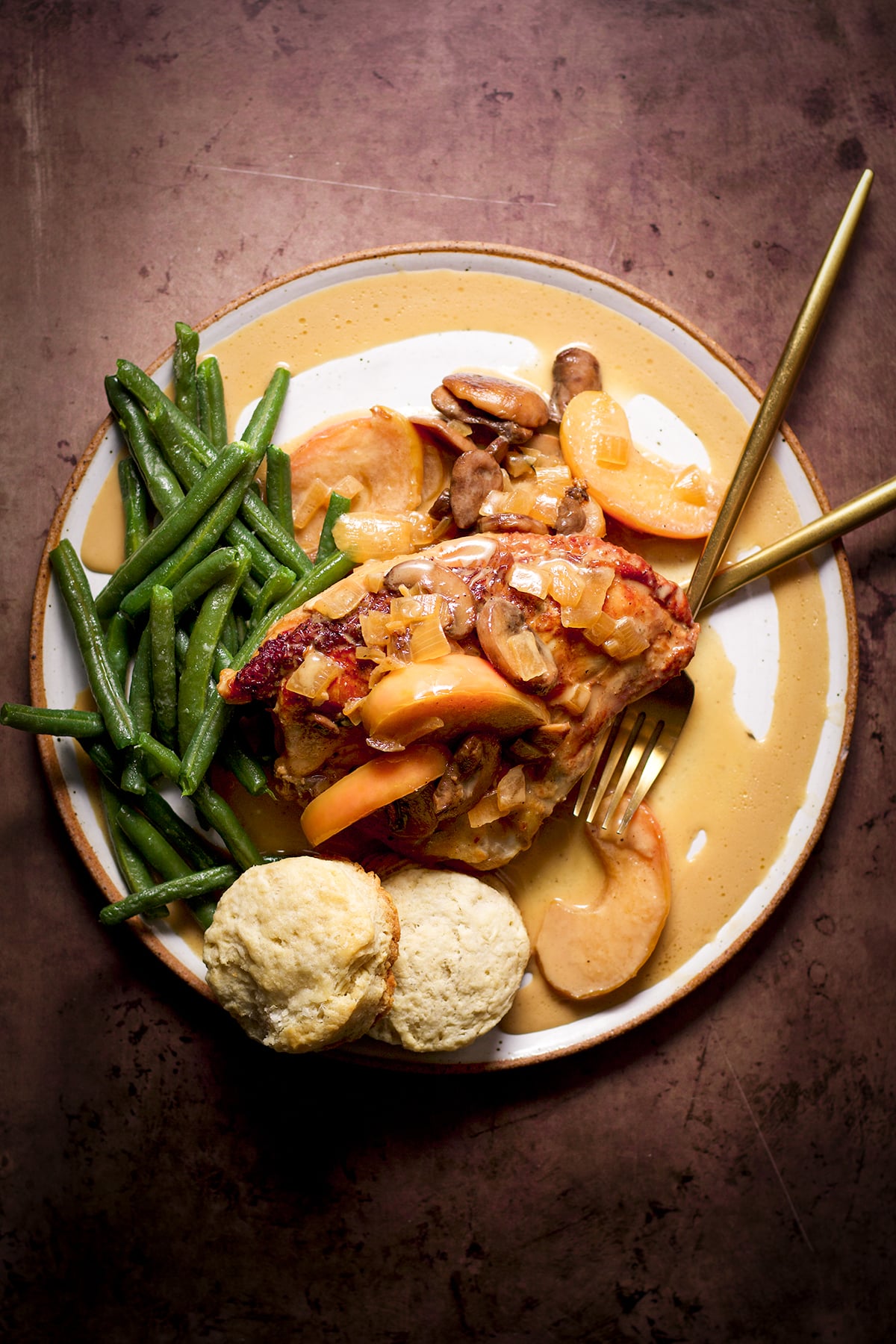 A serving of chicken and apples with cider cream sauce and green beans on a dinner plate.