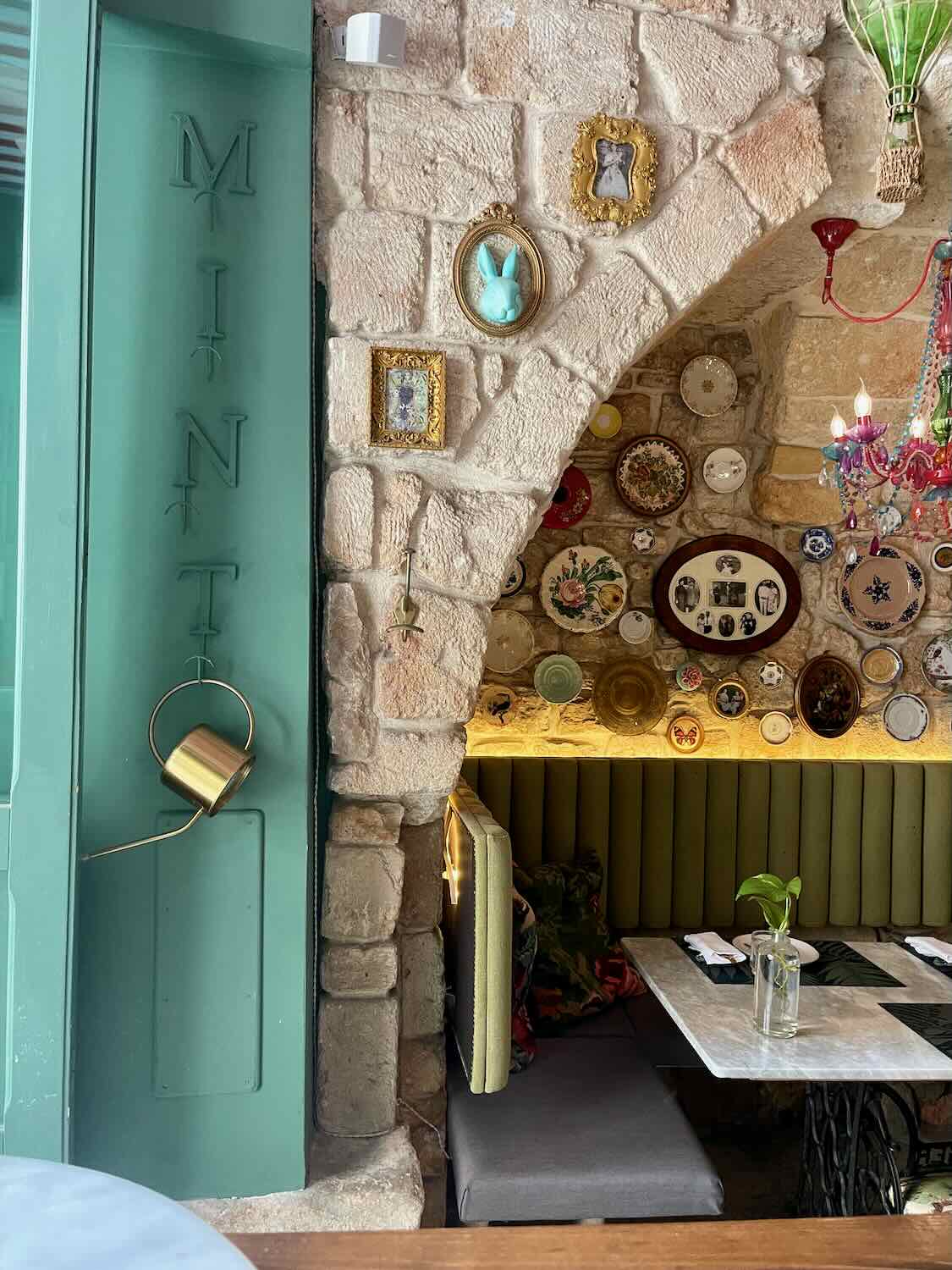 A detailed view of the decor at Mint Cucina Fresca, including framed art pieces, decorative plates, and a blue wall-mounted bunny head. The stone walls and arched seating area create a charming atmosphere.