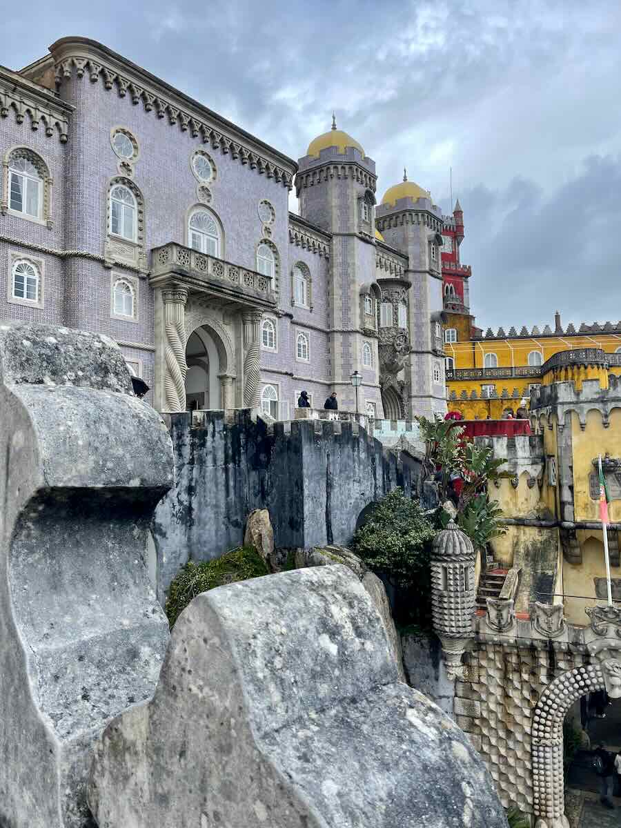 A close-up view of the colorful Pena Palace in Sintra, Portugal, showcasing its intricate architecture, grand towers, and stunning tilework. The yellow and red turrets stand out against a cloudy sky.