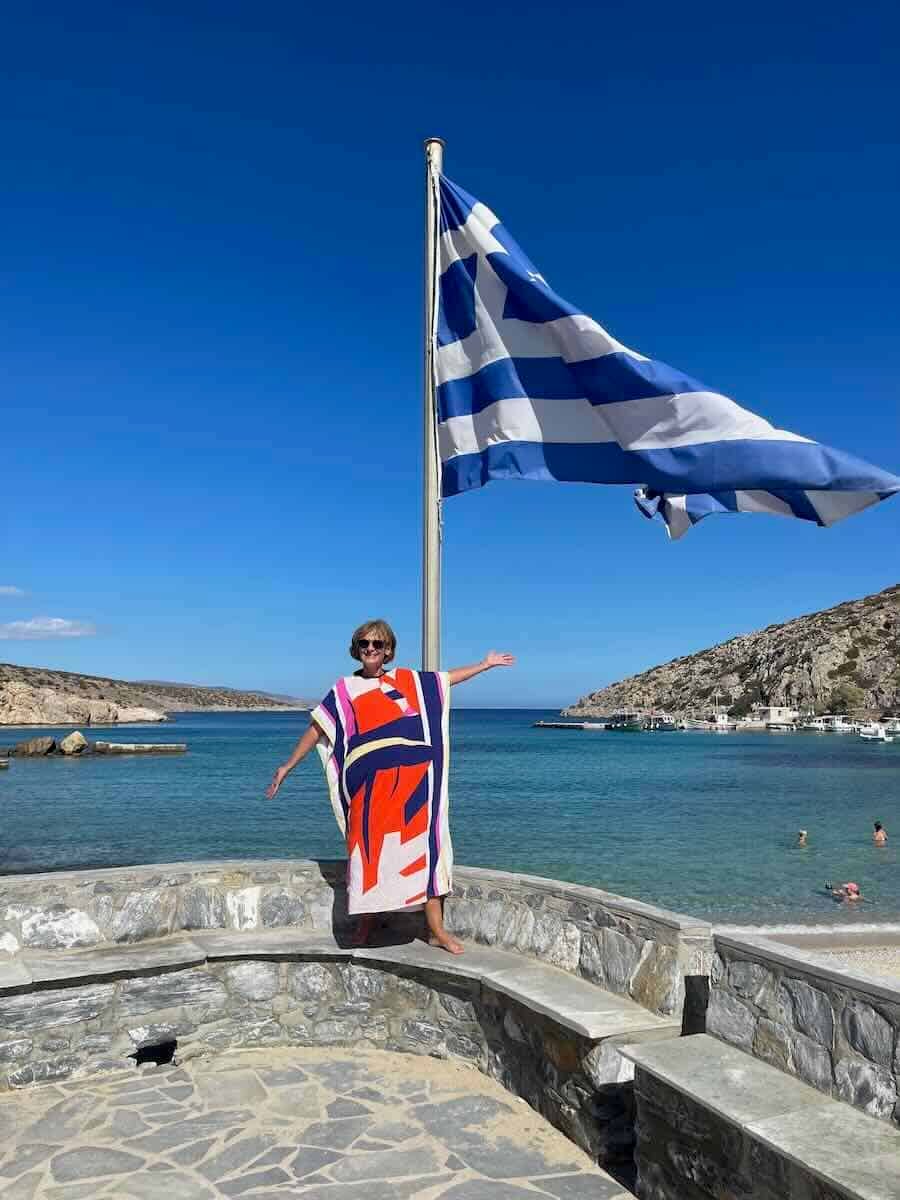 Woman standing on the ledge of a bench under the Greek Flag.