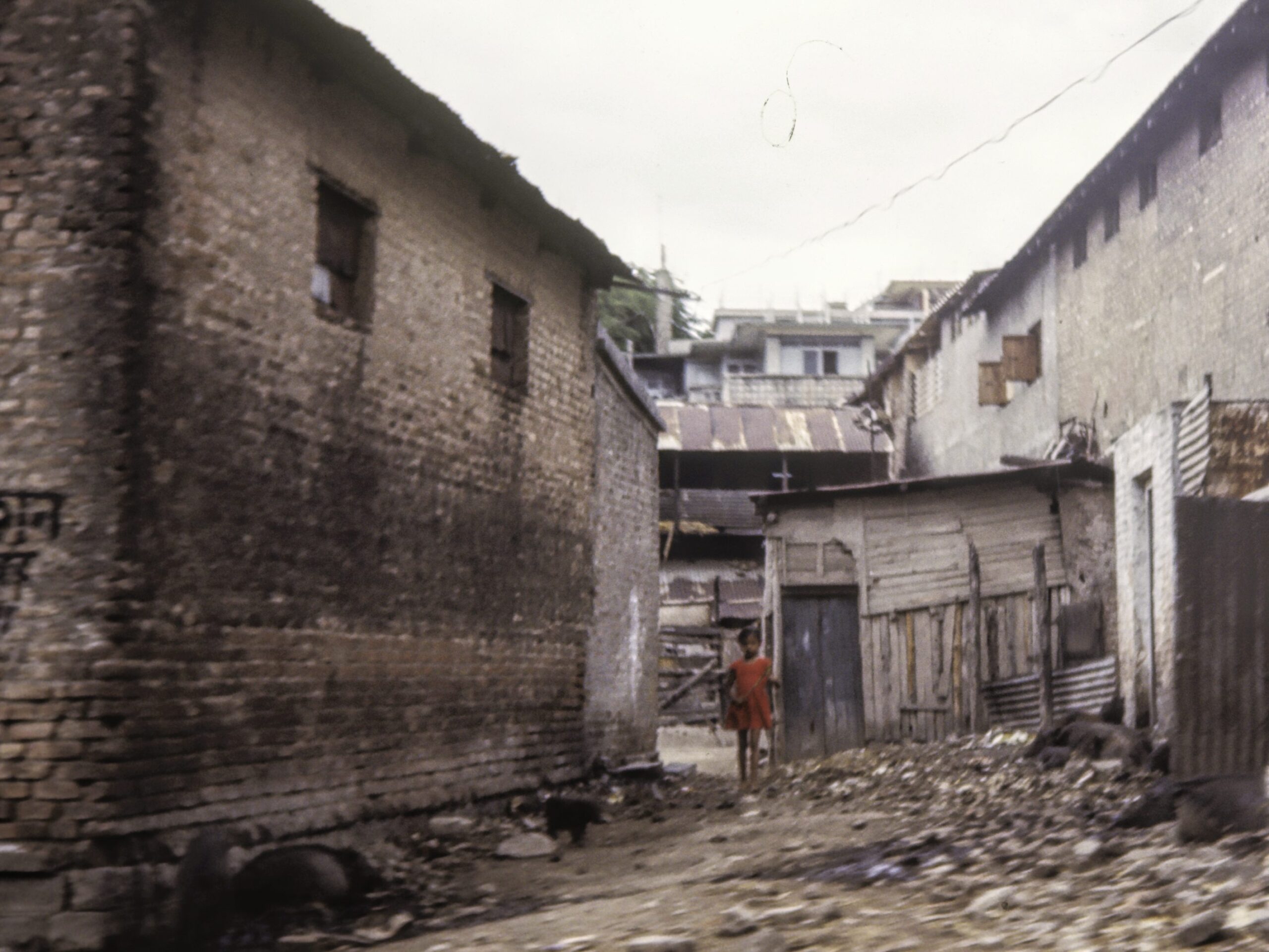 A young Indian girl in a red dress in a run down housing area