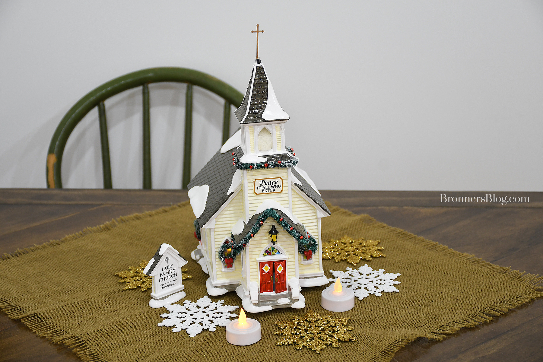 "Holy Family Church" displayed on table atop burlap with gold and white snowflakes and battery-operated tea lights
