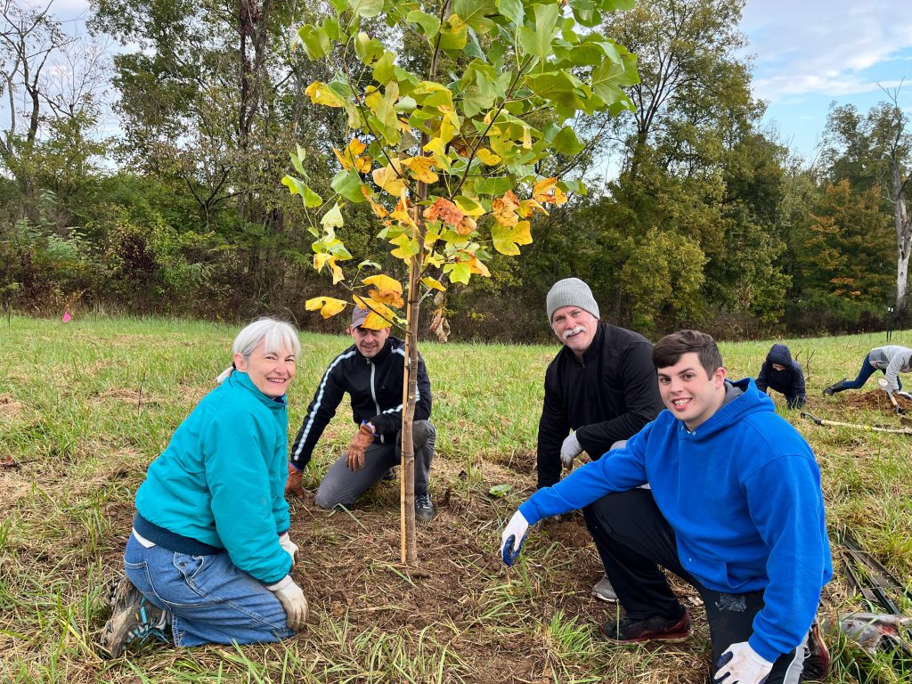 A group of volunteers pose with the young tree they planted at Mitchell Memorial Forest on October 23, 2021.