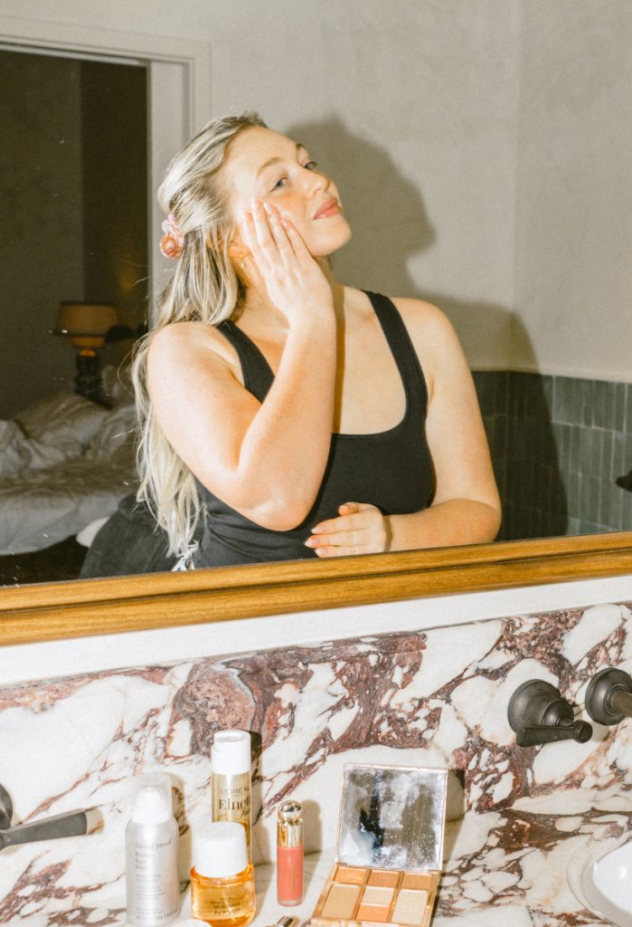 Woman applying skincare in mirror.