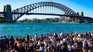 Gente bebiendo y comiendo en los restaurantes y bares alrededor de la Ópera de Sydney y el Harbour Bridge, Sydney, Australia.