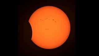 un sol parcialmente eclipsado con la luna apareciendo a la izquierda