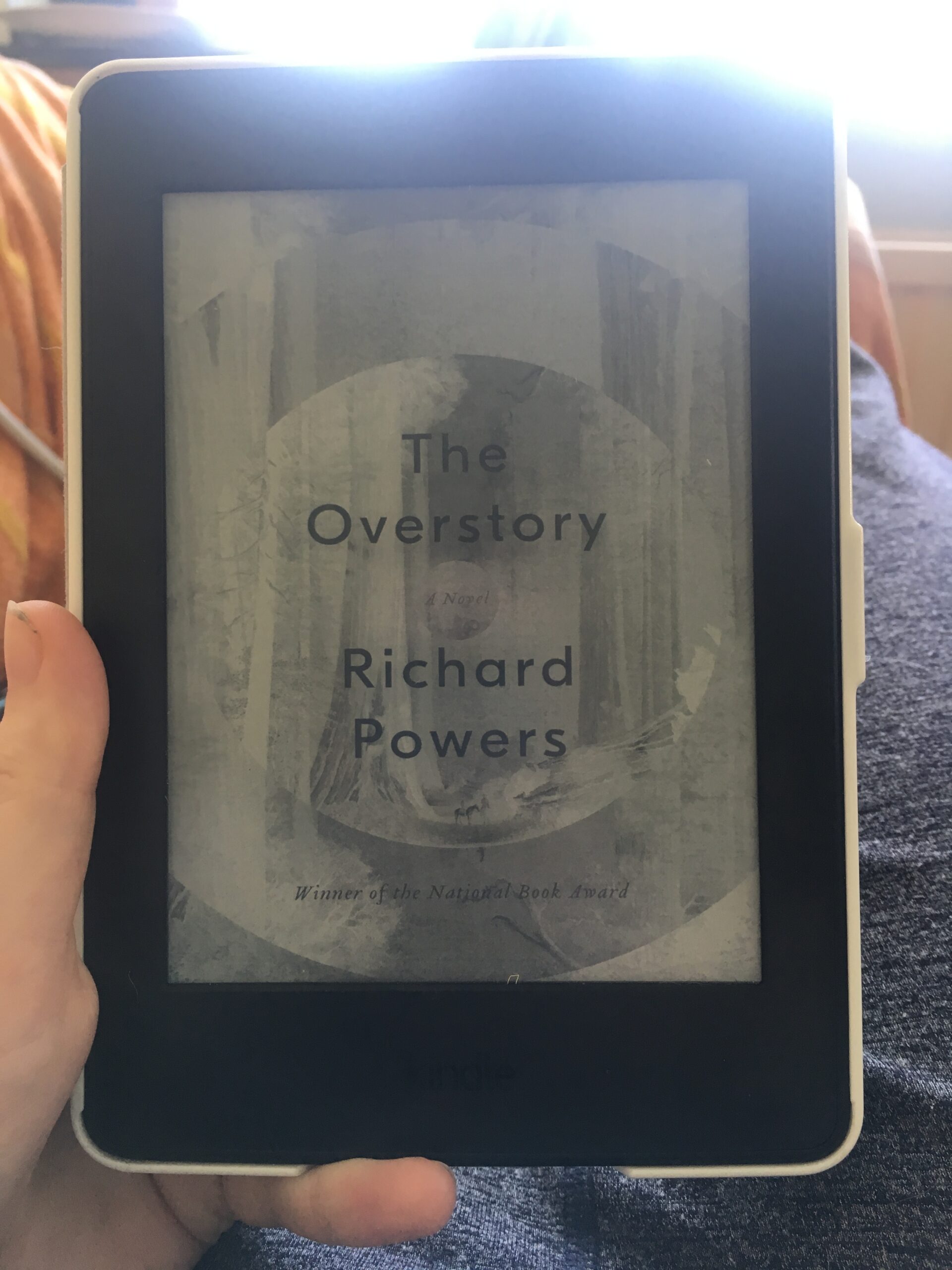 This is a kindle, with the front cover of The Overstory by Richard Powers on it in black and white.