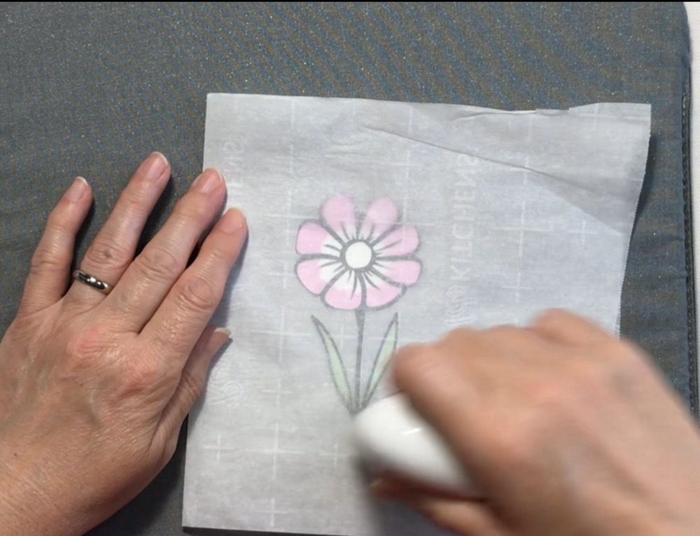 Photo showing the process of useing the Cricut EasyPress Mini  to adhere the HTV outline to the flower base between a folded piece of parchment paper. 
