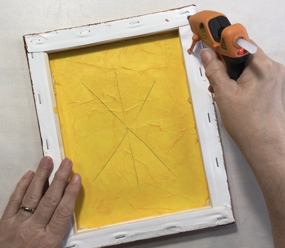 Photo showing the application of hot glue to the back of the canvas before adding the back board.