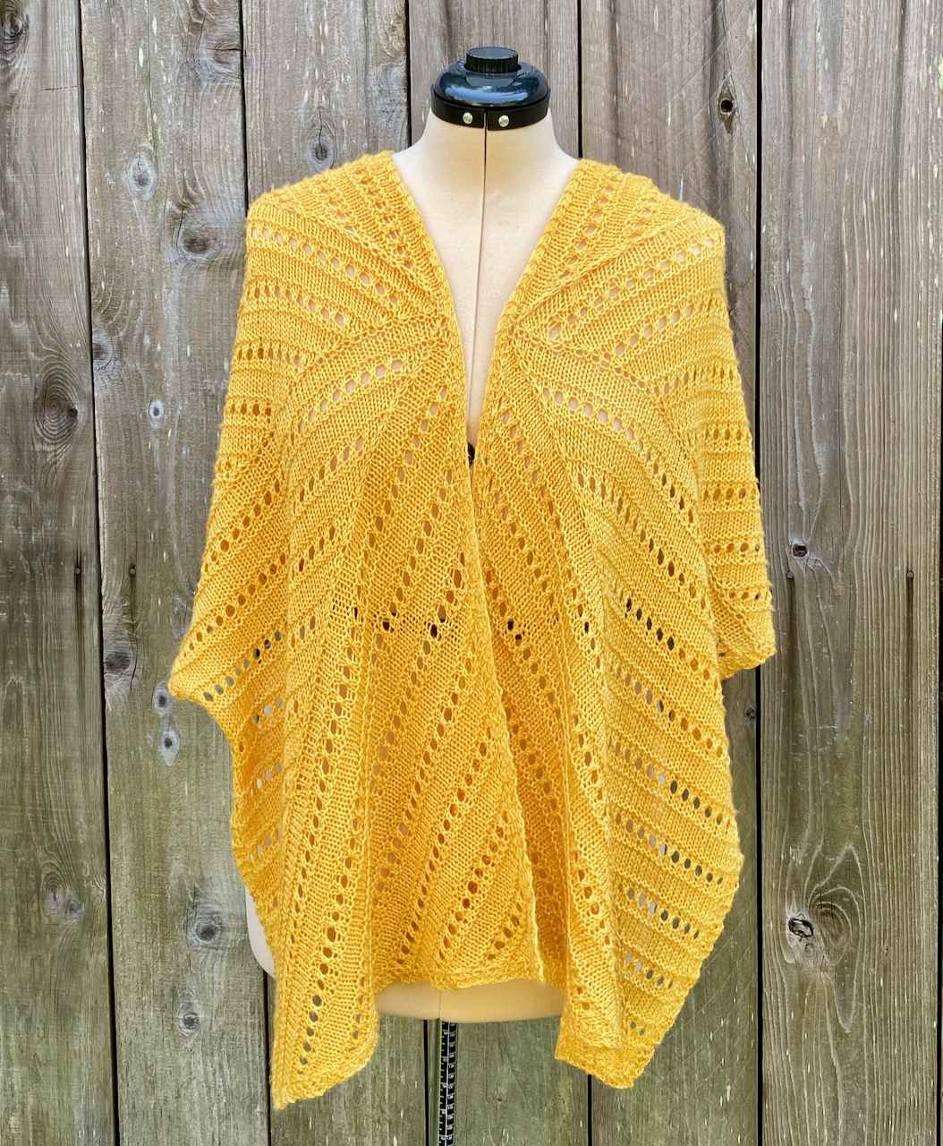 A golden hand-knit lace wrap is draped around a dressmaker's dummy.