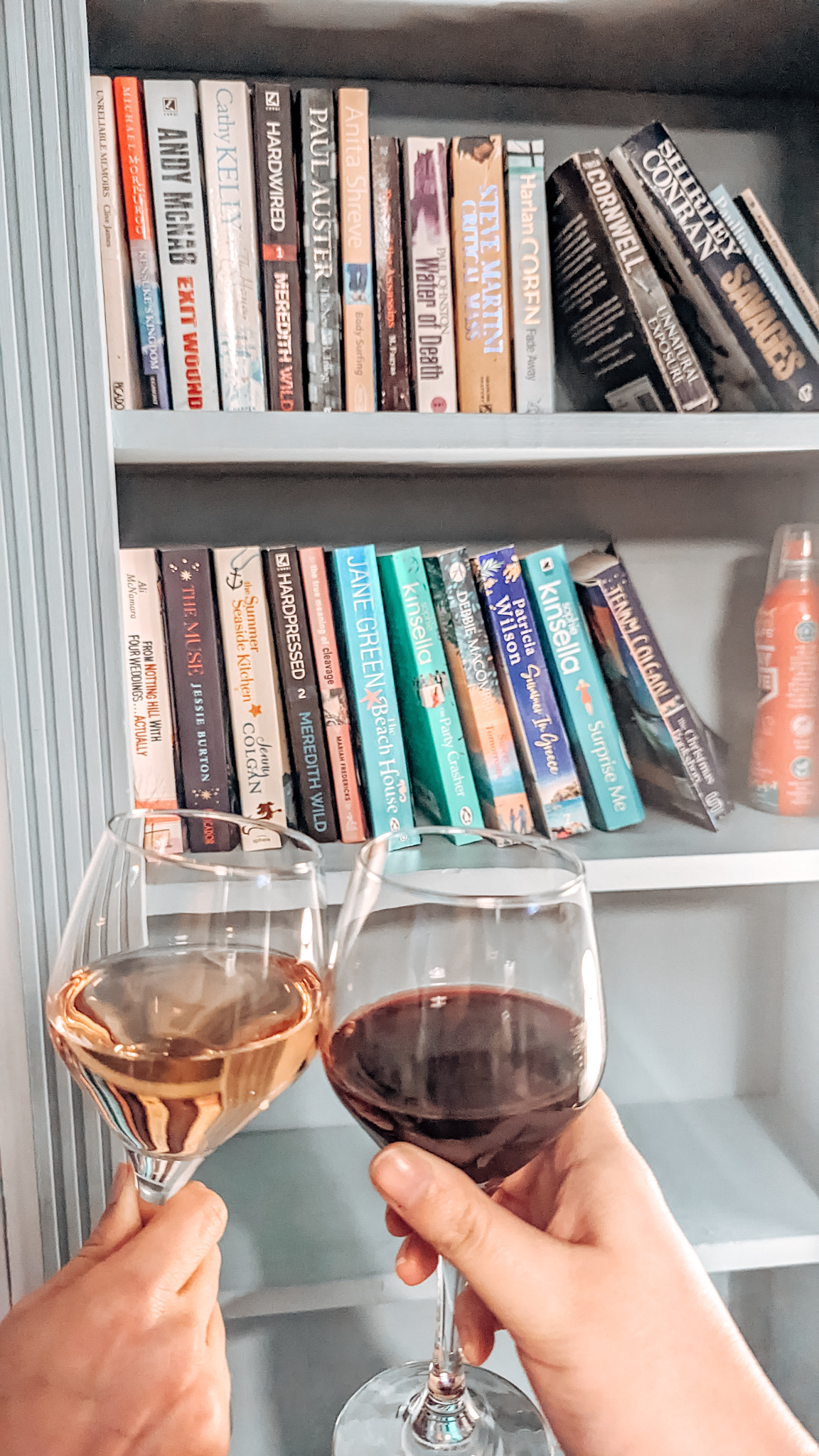Cheers! Louise and Sam clinking their wine glasses together in front of a bookshelf filled with colourful books