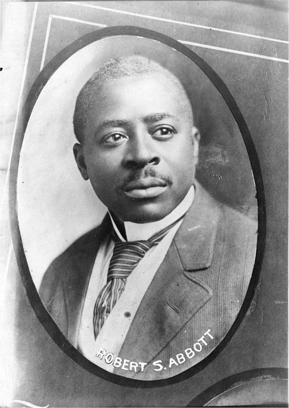 Black & white portrait-style photo of Robert Sengstacke Abbott from the chest up in an oval frame. He is dressed in a formal tailored suit jacket, white dress shirt and tie.