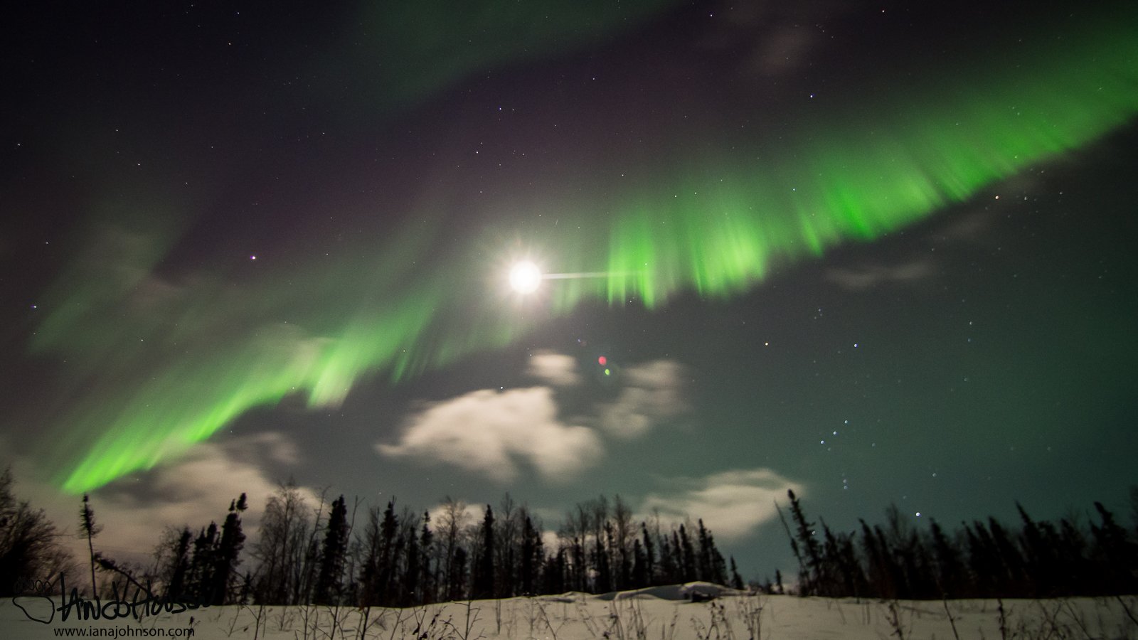 A brilliant green curtain of aurora stretches across the moon.