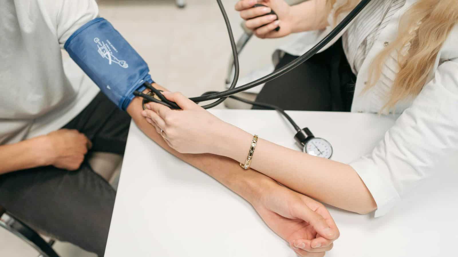 A healthcare professional is measuring the blood pressure of a seated person using a sphygmomanometer. The professional is holding the person's arm steady while the cuff is wrapped around the person's upper arm. The scene is set in a clinical environment.