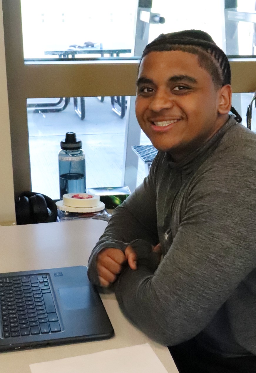 a smiling young man sits at a table with a laptop