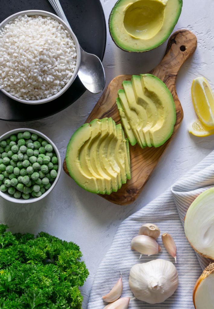 sliced avocados, a bowl of arborio rice, parsley, frozen peas, and garlic