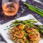 scallops over mushroom risotto on a white plate with asparagus