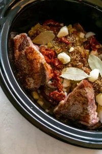 Barbacoa ingredients in a slow cooker with seasonings added.