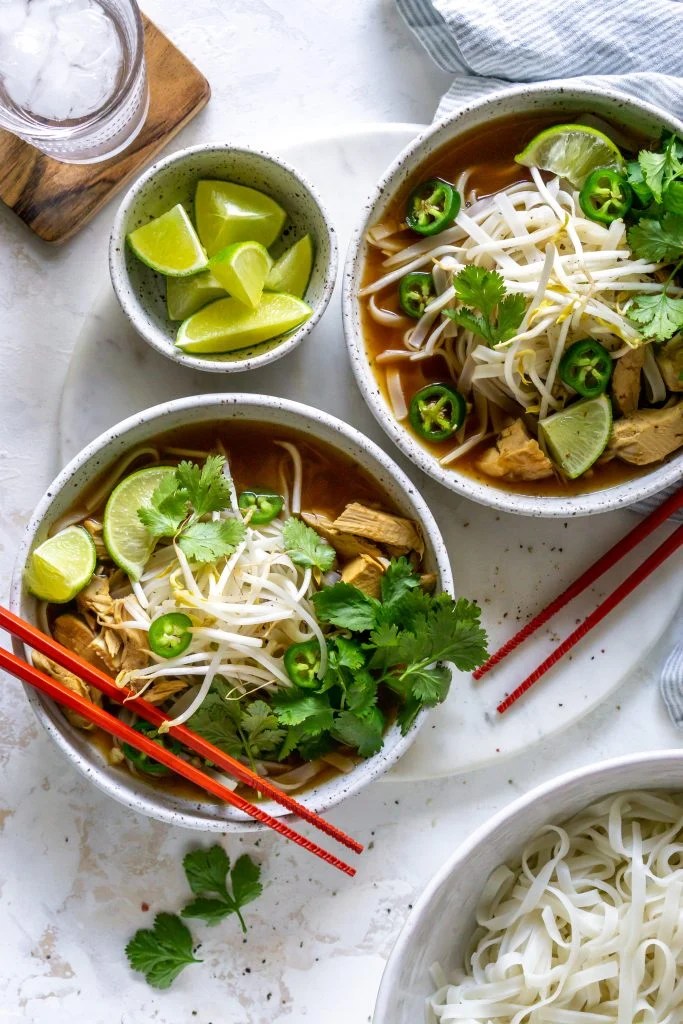 two bowls of pho, glass of water, and bowl of limes