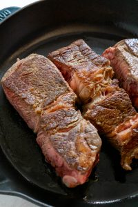 Barbacoa beef seared in a cast iron skillet until browned.