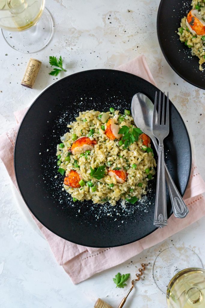 two black plates with lobster risotto and white wine