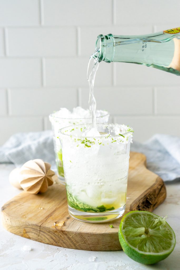 pouring seltzer water over mojitos