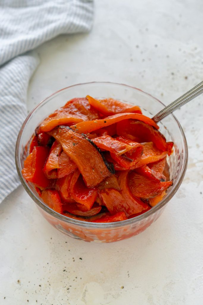 sliced roasted red peppers in a glass bowl with a spoon