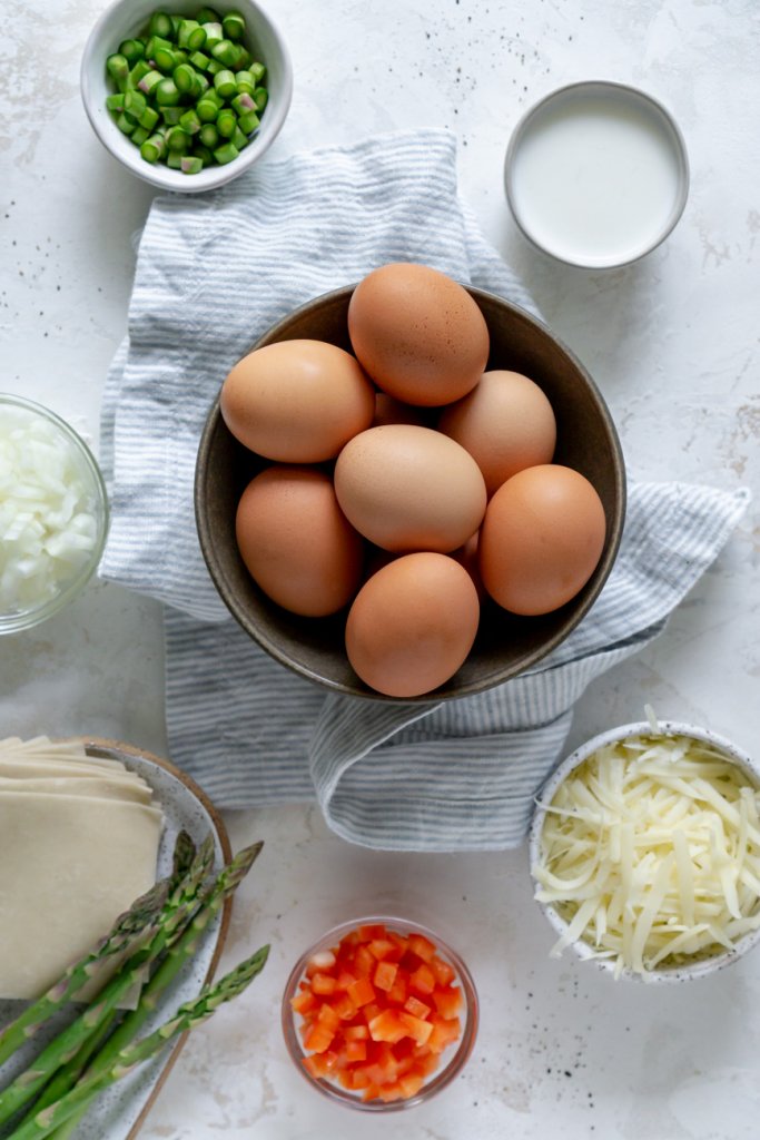 ingredients in small bowls: eggs, peppers, onions, wonton, asparagus, milk