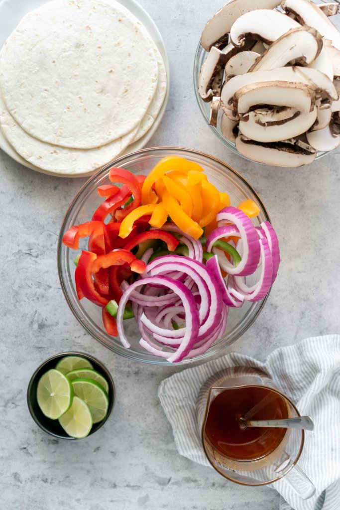 ingredients in bowls: peppers, onions, limes, mushrooms
