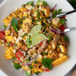 avocado corn salad in a white bowl with lime wedges
