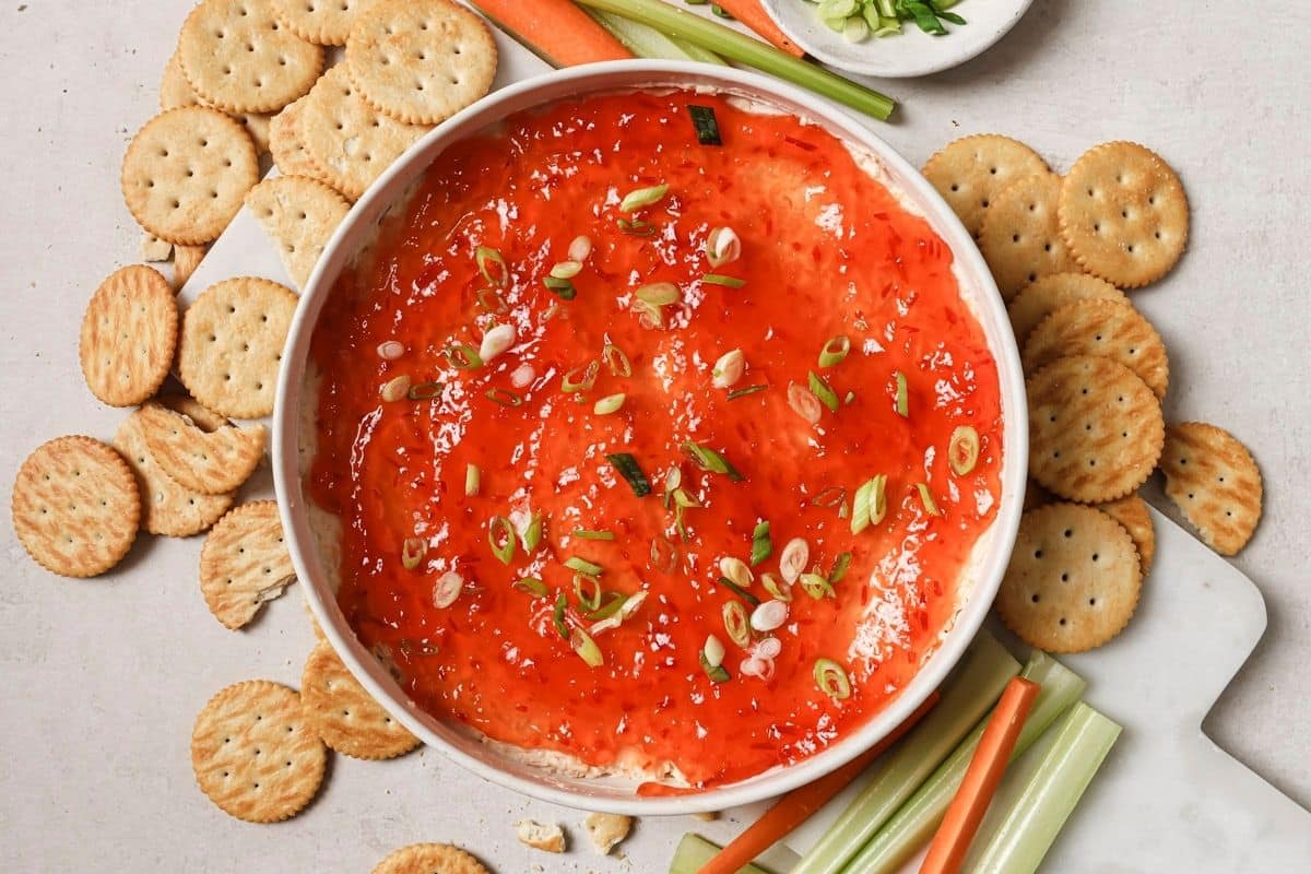 Red pepper jelly dip with crackers and celery and carrots.