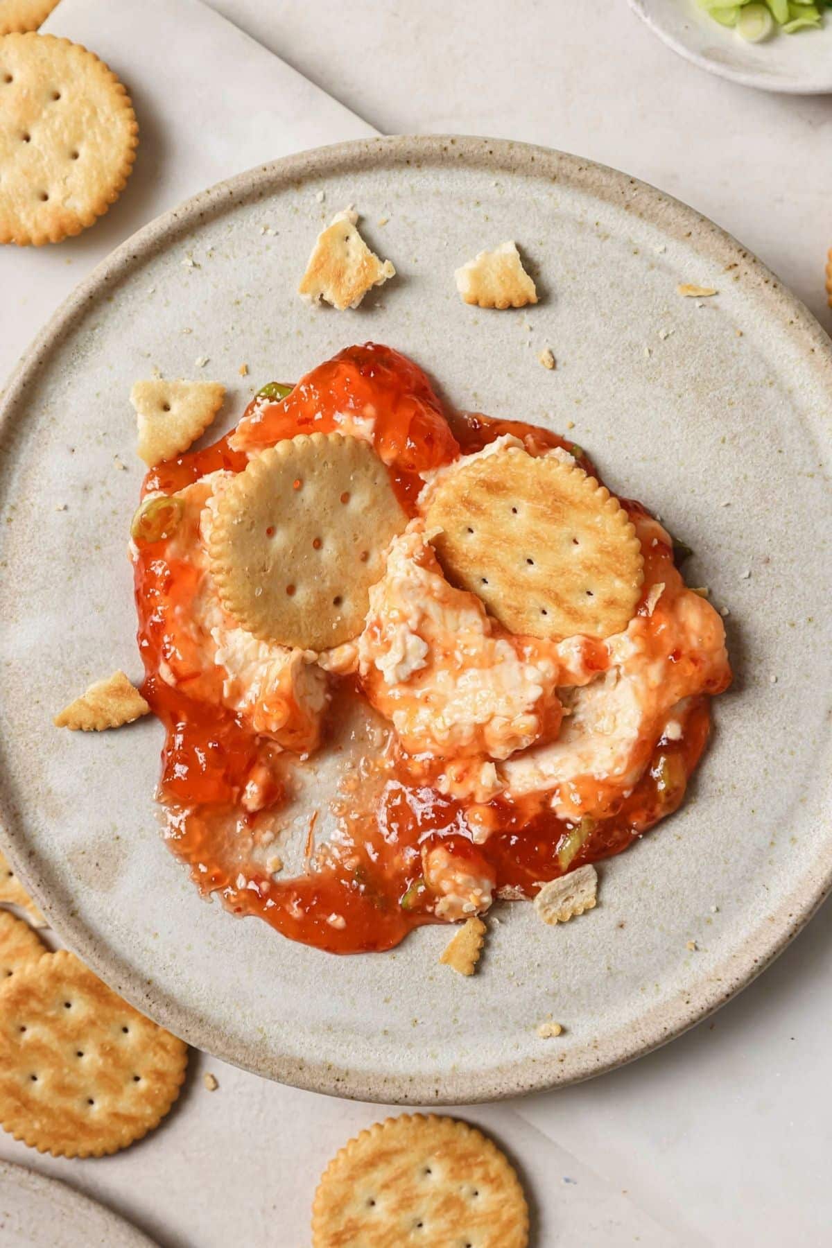 A serving of red pepper jelly dip with a cracker on a tan plate.