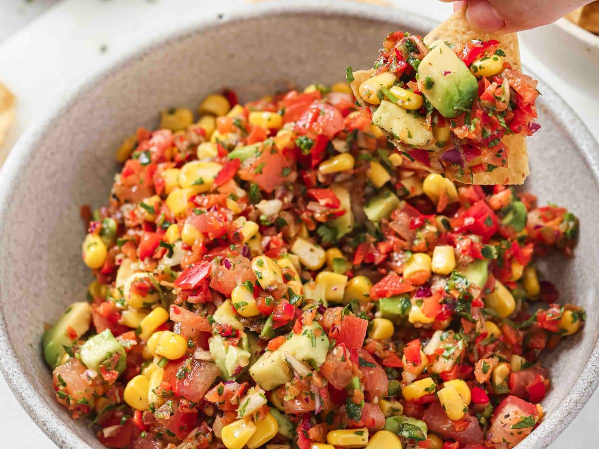 A spoon holding a scoop of corn salsa with avocado showing the various textures and ingredients. 