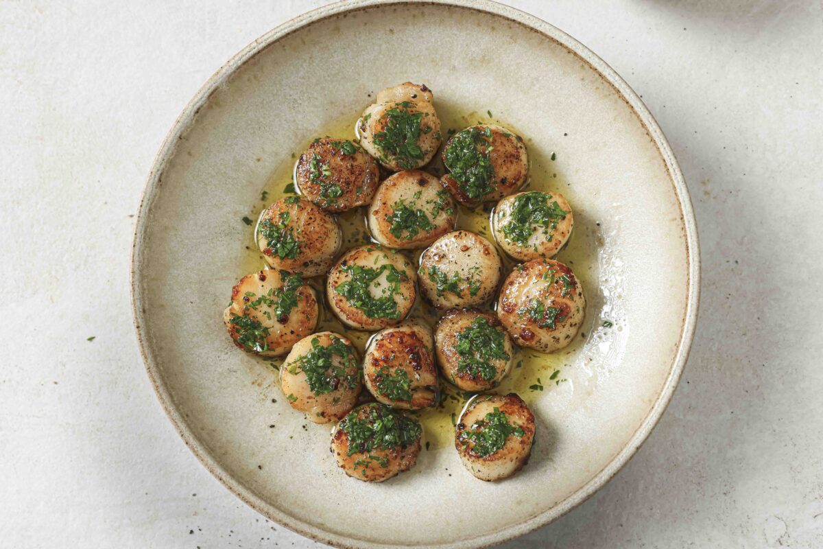 Pan-seared scallops finished with parsley butter in a bowl on a white countertop.