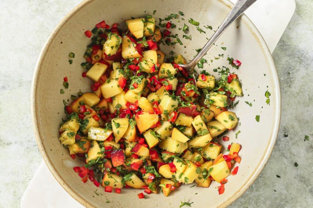 Salt mixed into the peach salsa and a spoon combining all of the ingredients together. 