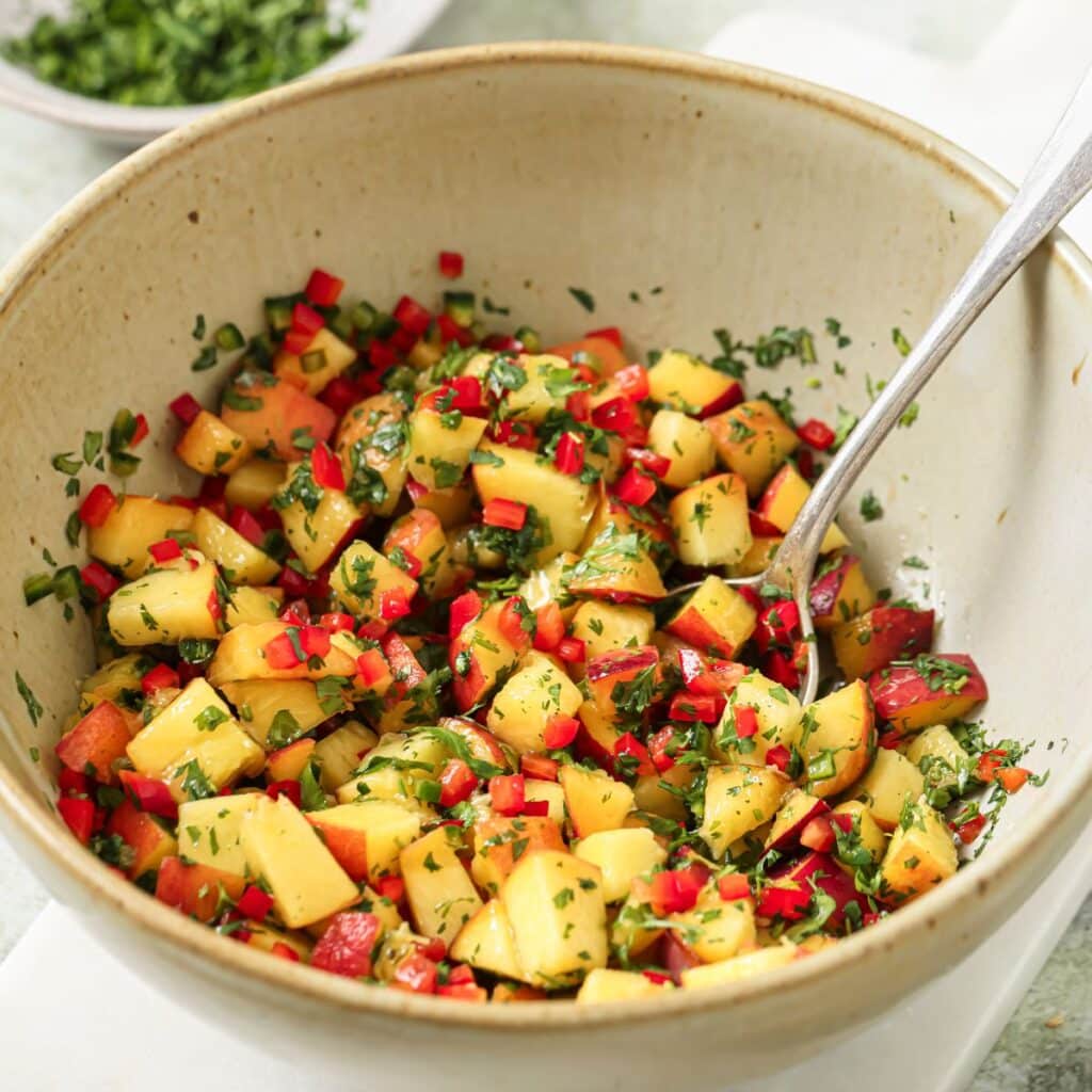 A bowl of peach salsa with a spoon resting on the side.