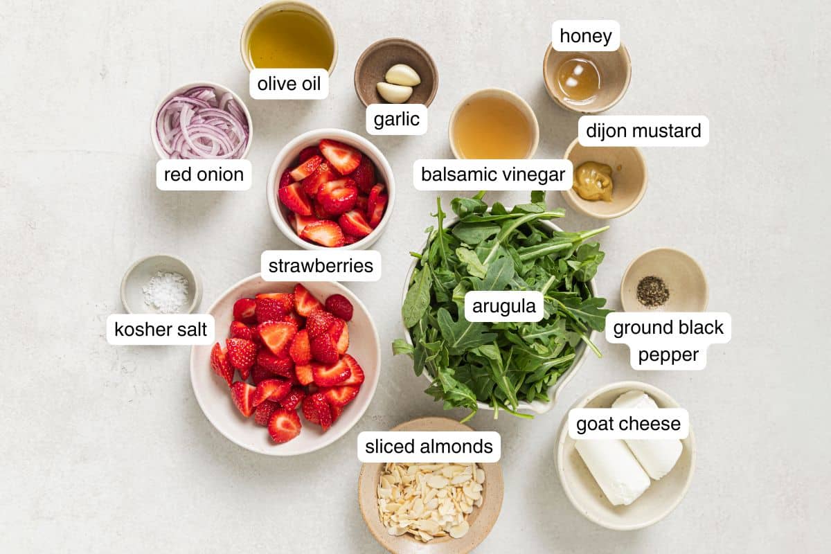 A flat lay of ingredients for strawberry arugula salad labeled on a countertop.