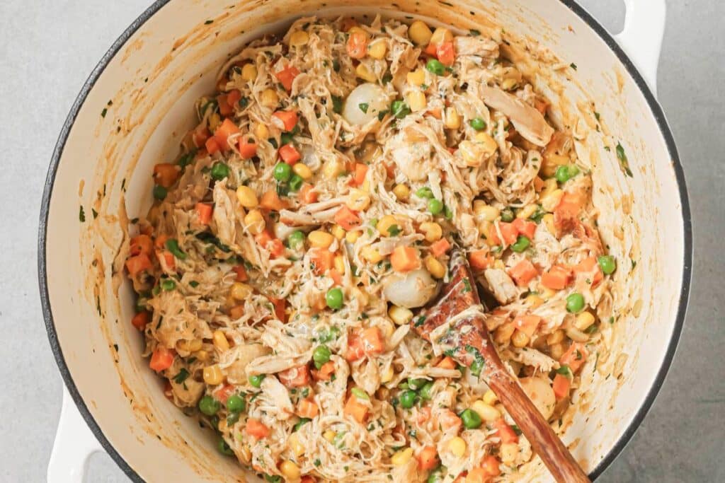 Adding the chicken, onions, peas, and carrots to the chicken pot pie filling.