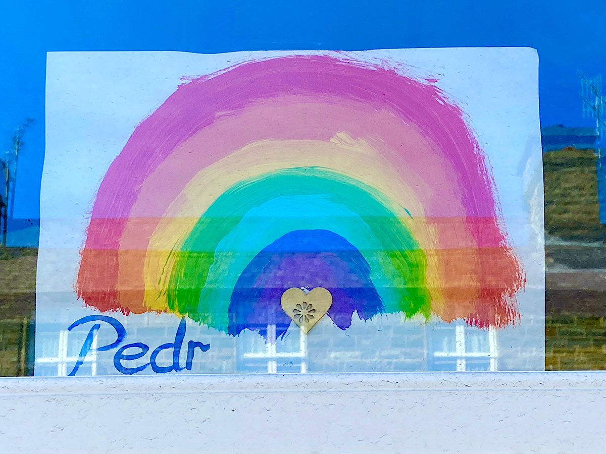 A rainbow in a window with Pedr in the corner and a small wooden heart in the middle