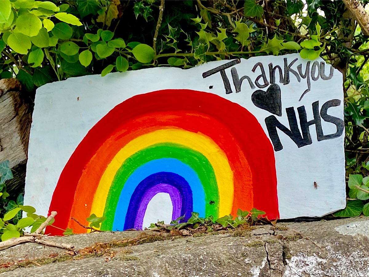 Thank you NHS is written in the corner of a large rainbow painted onto a large white piece of rock by the side of the road