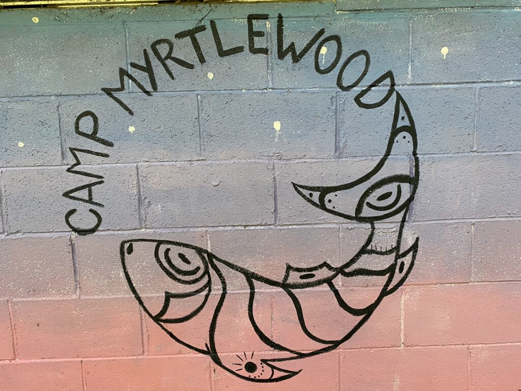 Camp Myrtlewood Logo incorporating stylized salmon and text
