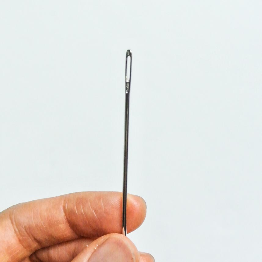 Eye of needle held over white background. Tips for threading needle