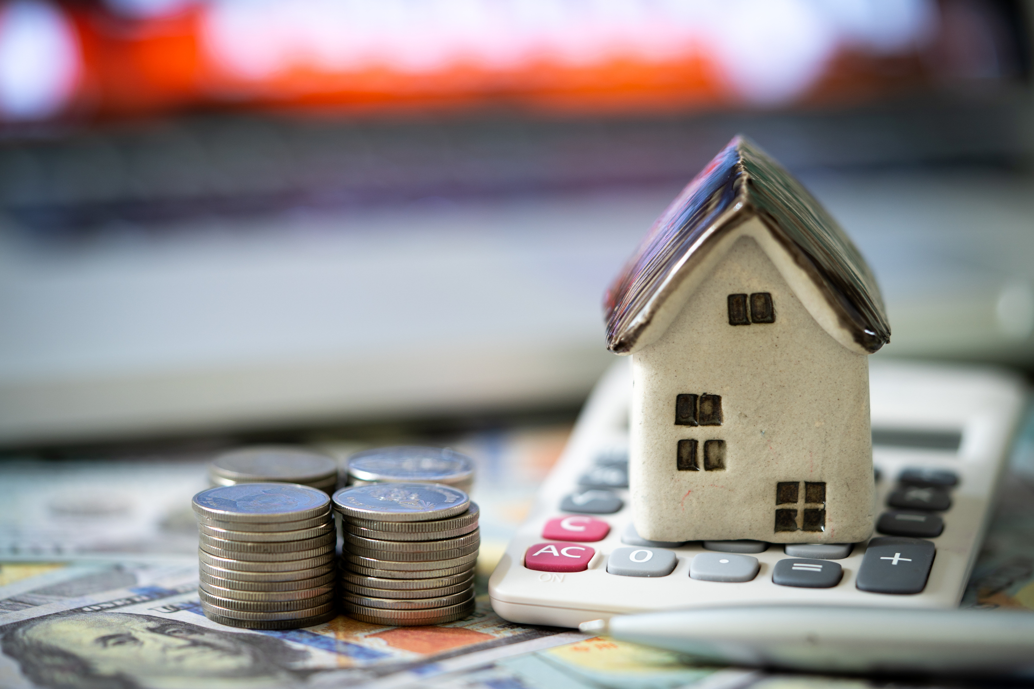 a small model of a home rests on a calculator next to stacks of coins