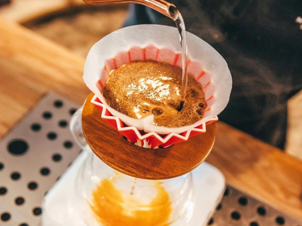 A barista brews black coffee in a red Origami brewer.