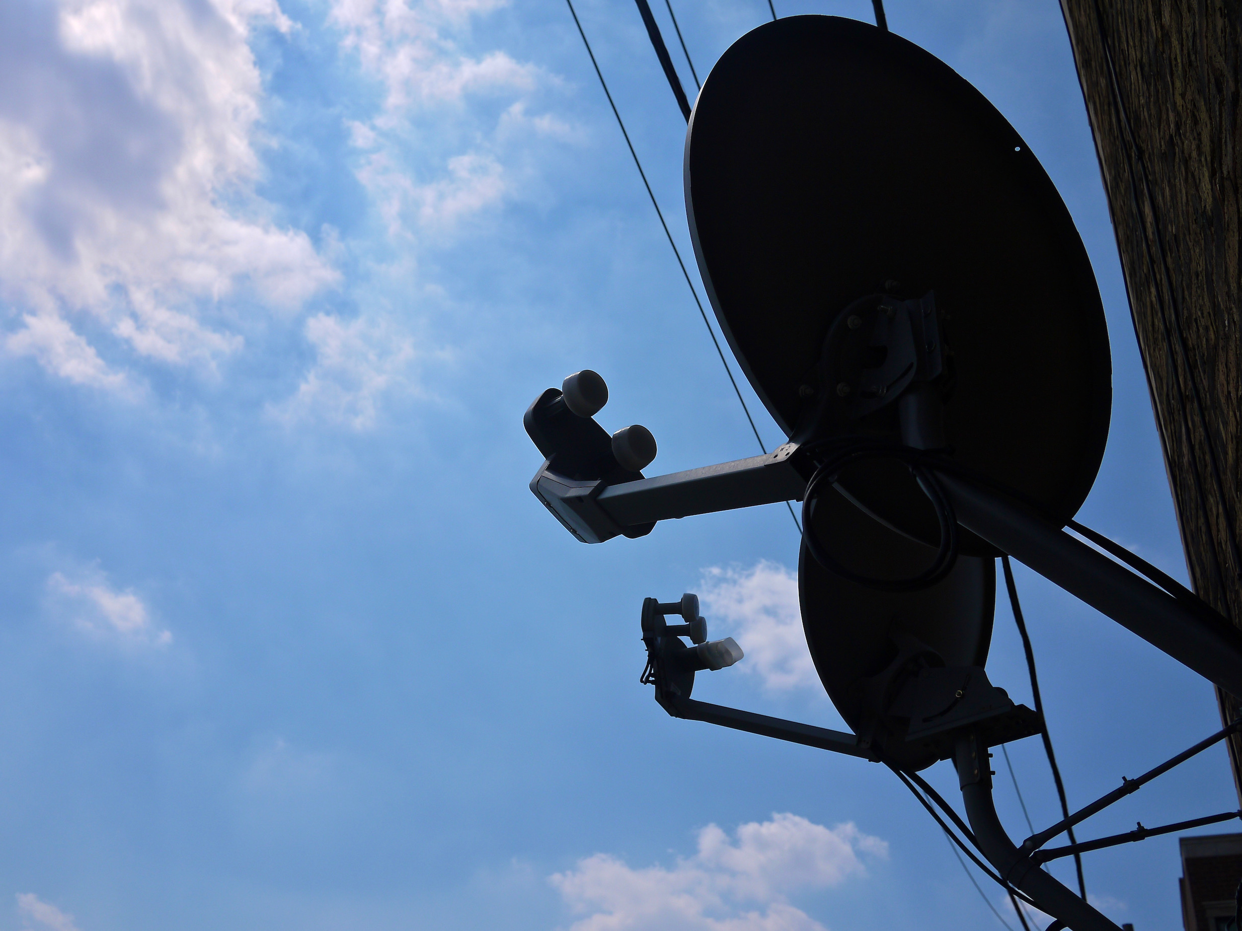 A silhouette of a TV satellite dish with a cloudy sky behind it.