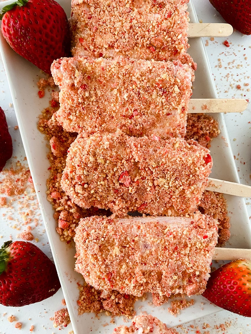 homemade strawberry crunch ice cream bars arranged in a row on a white serving platter