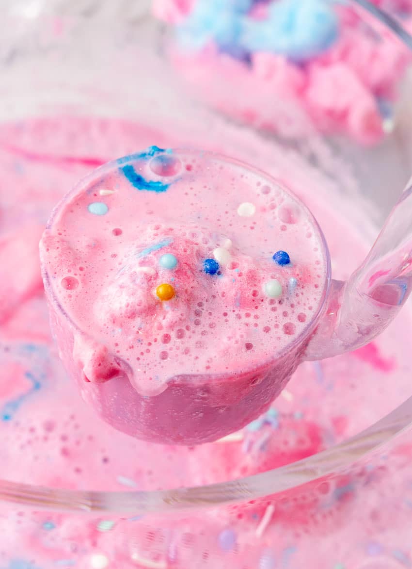 a clear plastic ladle holding up a scoop of unicorn party punch topped with colorful sprinkles