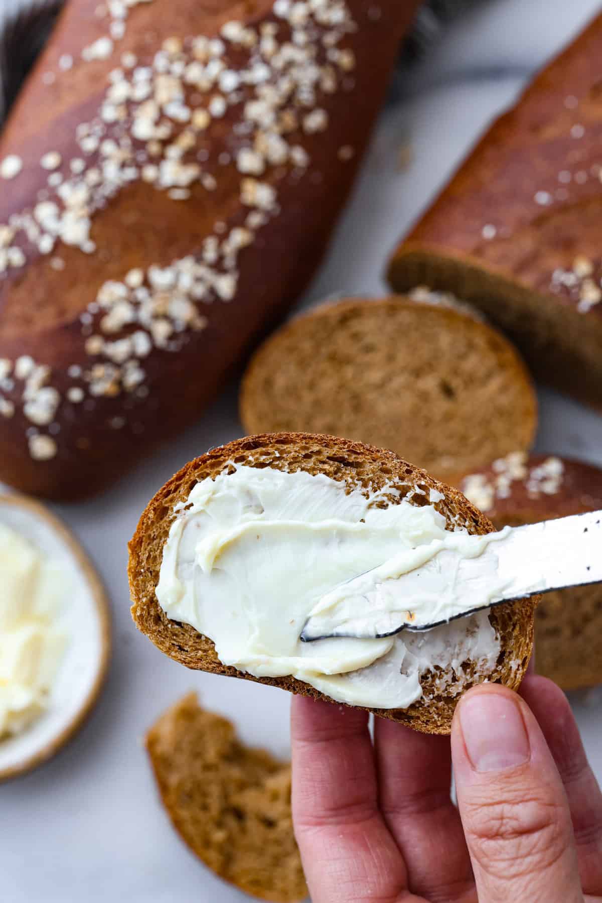 Make this copycat version of the EPIC Cheesecake Factory brown bread that is loved and devoured by all who dine at this incredible American restaurant. The rich brown color comes from the molasses, honey, whole wheat, espresso, and cocoa powder. These unique ingredients create the tastiest bread that no one can resist! Close view of butter being spread onto a slice of brown bread.