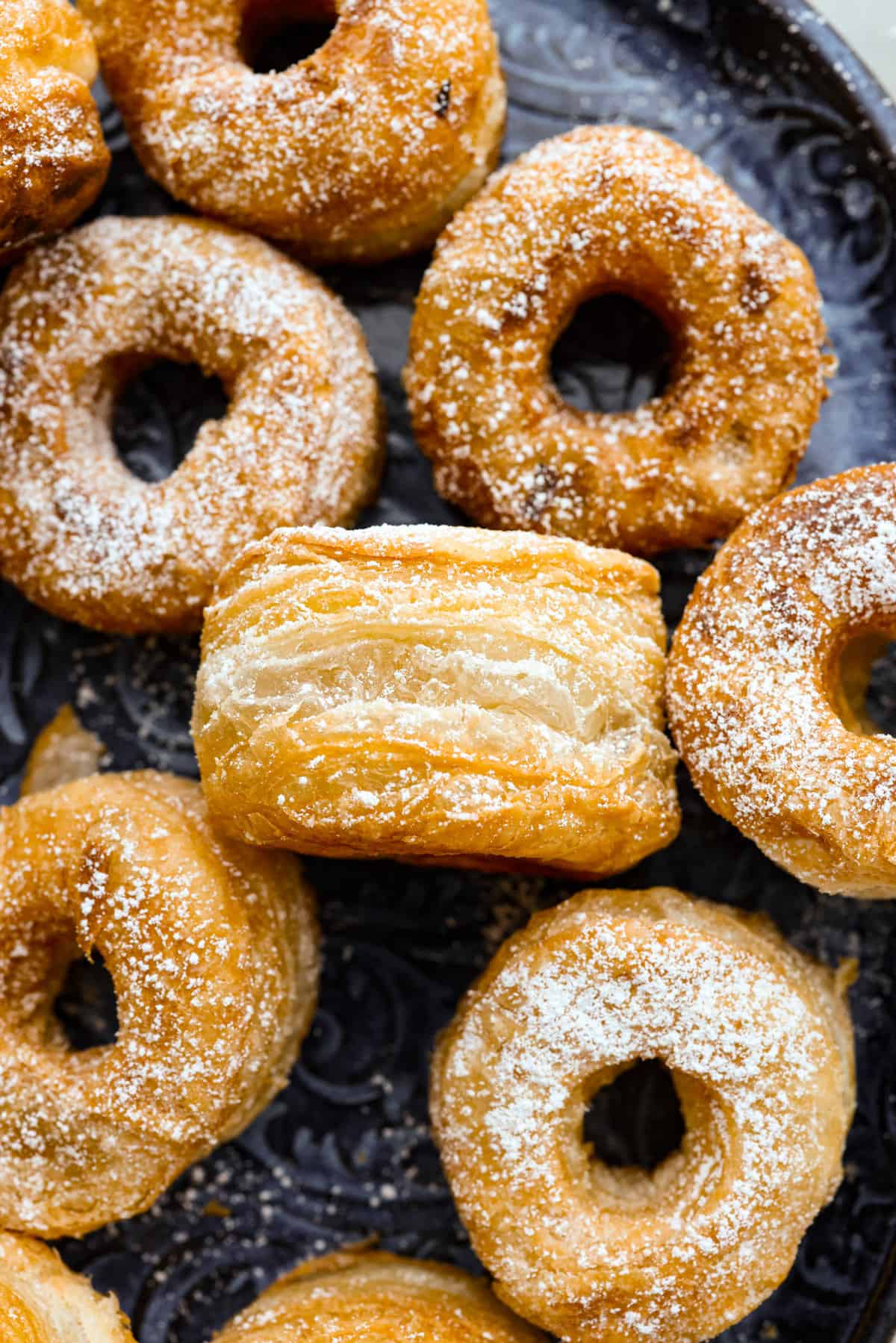 Get ready to discover the joy of homemade cronuts with this delicious recipe! Perfectly flakey and fried, this easy-to-make recipe is perfect for any occasion. The close up of a cronut on its side so that you can see all of the layers.