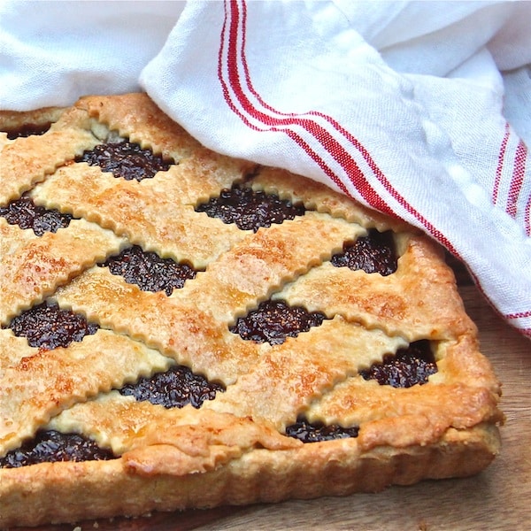 A fig crostata fresh from the oven with a lattice top and a red and white tea towel over one corner.